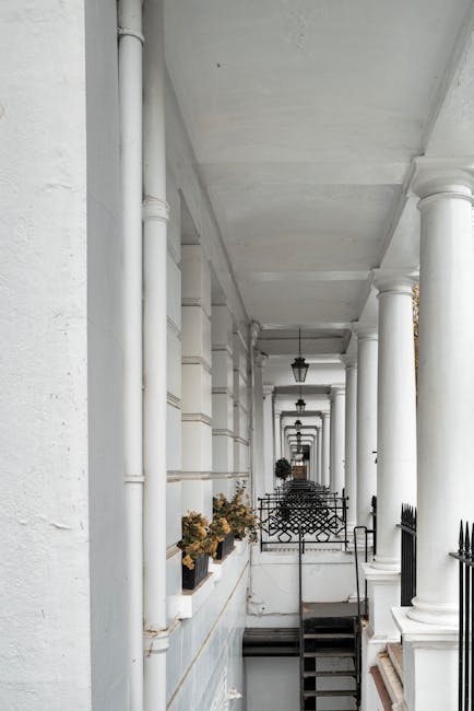 A row of elegant, multi-storey Georgian-style terraced buildings with cream and beige facades and white window frames lining a busy street in South Kensington, near Gloucester Road, under a partly clo